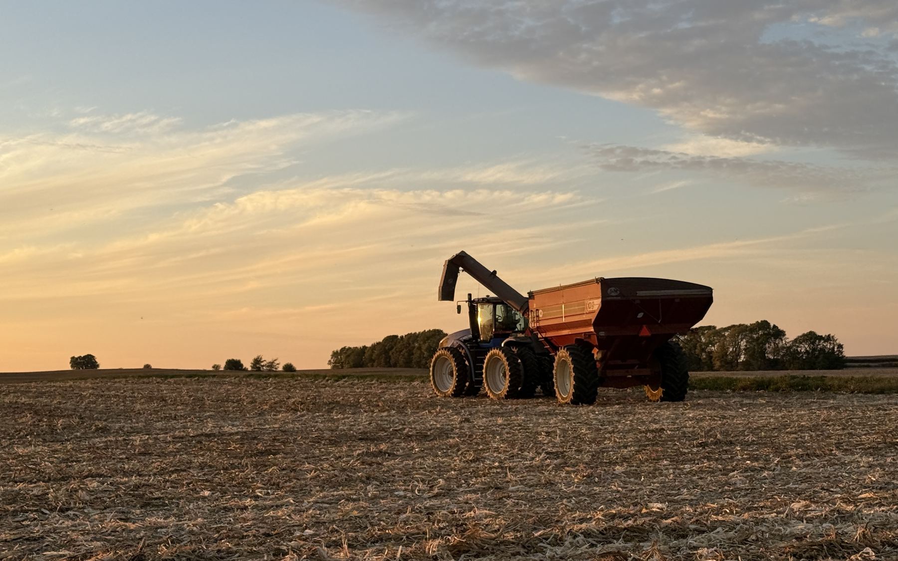 A tractor and grain cart parked on corn stubble at sunset in central Illinois